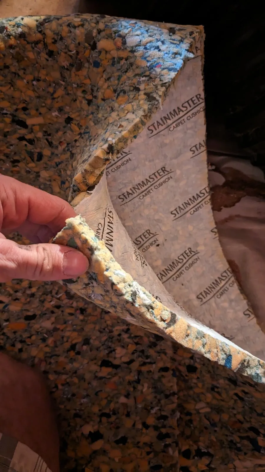 A hand holding up a piece of rebonded-foam carpet cushion